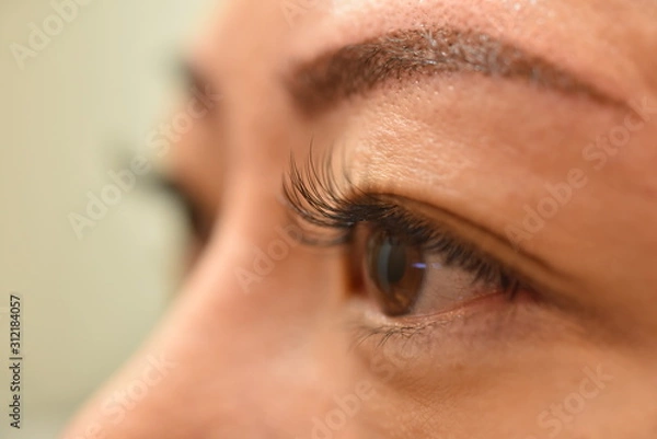 Fototapeta Asian woman got Eyelash Extension Service from skilled professional Lash Stylist to enhance length, curliness, fullness, and thickness of natural eyelashes. Fake lash applied one at a time using glue