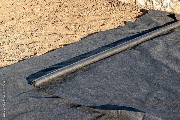 Fototapeta Woven geotextile fabric rolling out on the ground in the summer garden under reconstruction