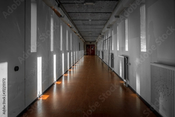 Fototapeta A long bare corridor with light and dark shadow spots. The corridor evokes an unpleasant and anxious feeling