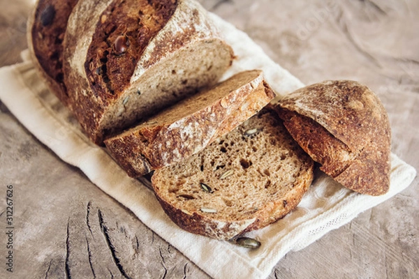 Fototapeta Brown fresh bread with seeds are cut into pieces on old wood background. Copy, empty space for text