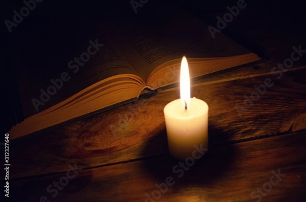 Obraz burning candle and a book on a table in the dark on a wooden table. Concept of knowledge, religion, magic