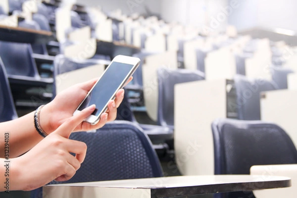 Fototapeta Female using phone in class and blur background of students during study or quiz, test and exams from teacher or in large lecture room / University classroom.