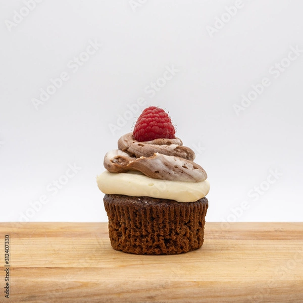 Fototapeta chocolate cupcake with frosting and raspberry garnish on wodden board