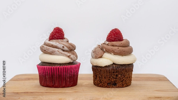 Fototapeta chocolate cupcake with frosting and raspberry garnish on wodden board