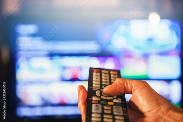 Fototapeta Hand mit Fernbediehnung vor großem TV Bildschirm auswählen / Online Streaming Netflix / Multimedia video wall television broadcast / Fernseh schauen