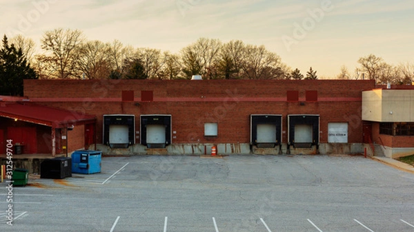 Fototapeta Establishing shot of an empty warehouse building with cargo loading dock and parking lot.