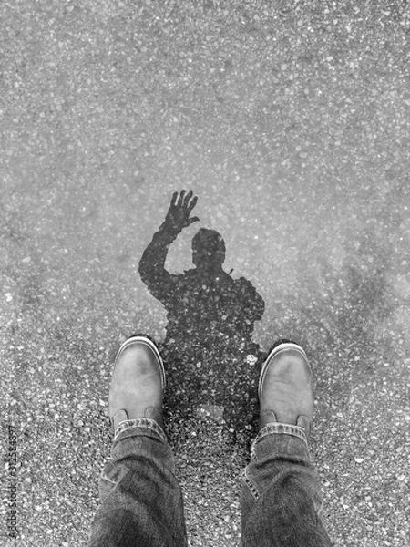 Obraz man waving hello to puddle and his reflection in silhouette is visible. Black and white.