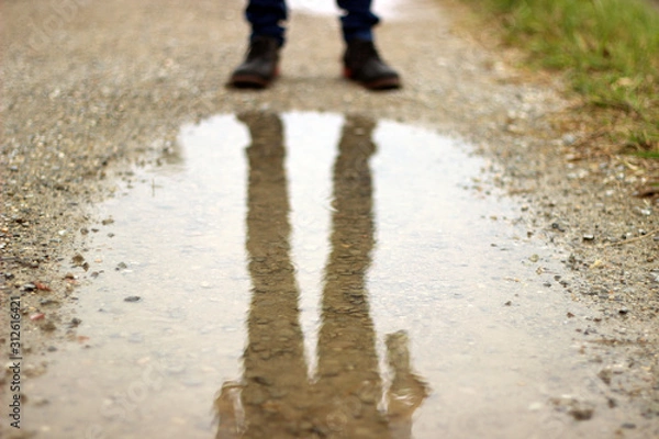 Obraz 土手道の水たまりに映るブーツとジーンズを履いた男性