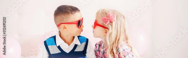Fototapeta Valentine day holiday celebration. Web header banner for website. Two happy Caucasian cute funny children wearing heart shape sunglasses. Boy and girl kissing. Love, friendship, fun.