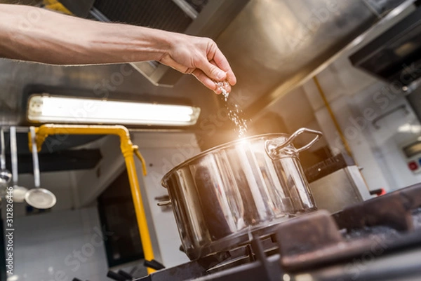 Fototapeta Man salting boiling water in pot on stove, closeup