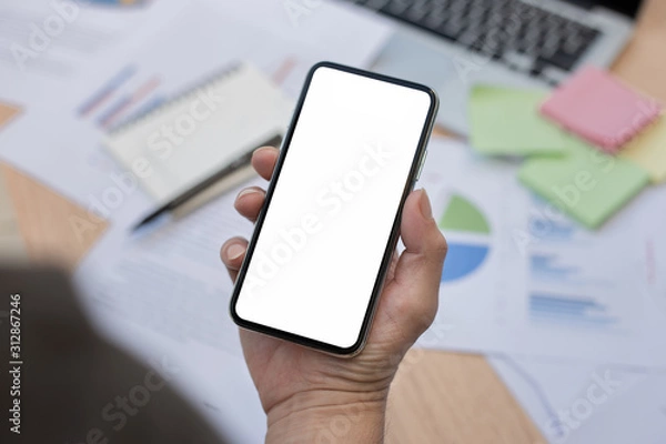 Fototapeta Mockup image blank white screen cell phone.man hand holding texting using mobile on desk at office.background empty space for advertise text.people contact marketing business,technology 