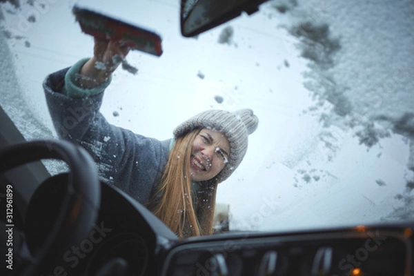 Fototapeta Girl with emotional face cleaning the windshield of a car from snow.