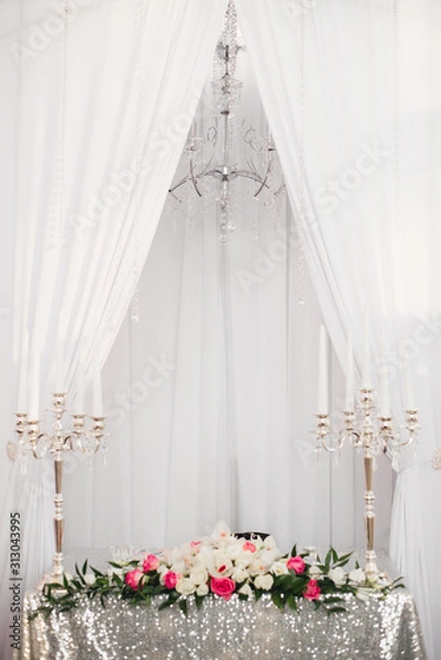 Fototapeta table with a tablecloth of silver sequins, two silver candelabra and a chandelier hangs over the table. Wedding decor for the bride and groom