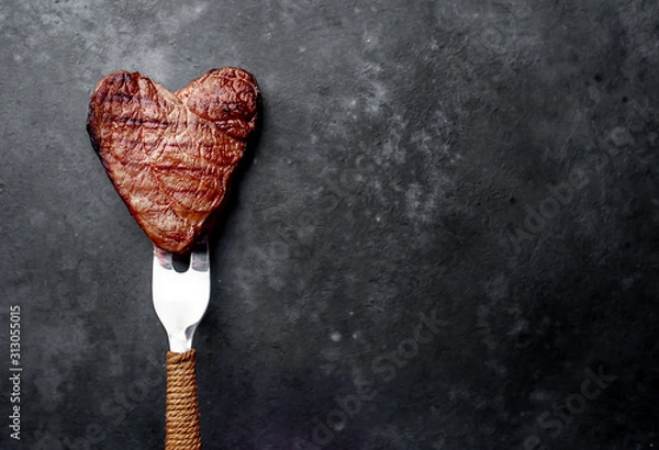 Fototapeta grilled beef steak in the form of a heart on a fork for Valentine's day on a stone background with copy space for your text
