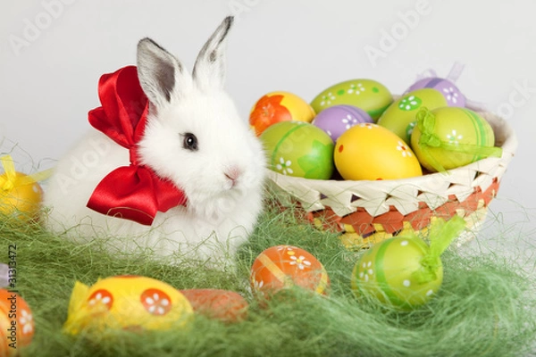 Obraz Easter bunny with red bow, sitting on grass, with colorful eggs