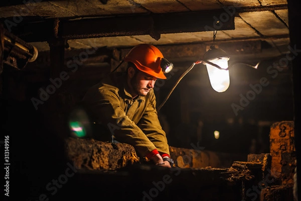 Fototapeta A tired miner in a coal mine looks at the light. Work in a coal mine. Portrait of a miner. Copy space.