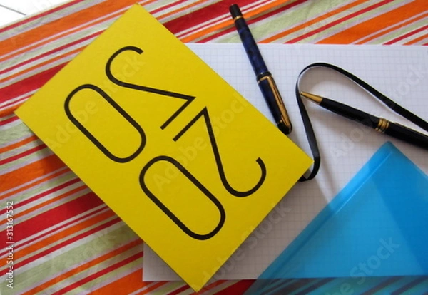 Fototapeta Yellow notebook organizer for 2020, two pens, a plastic blue file for documents and a checkered brulion on a colourful striped tablecloth