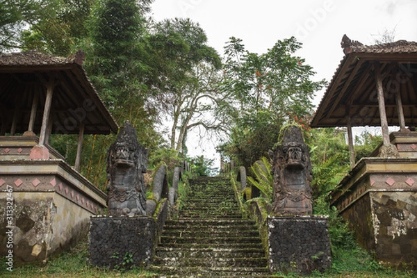 Fototapeta Balinese architecture. A large stone staircase on the street, overgrown with green plants. With two dragons on the handrails