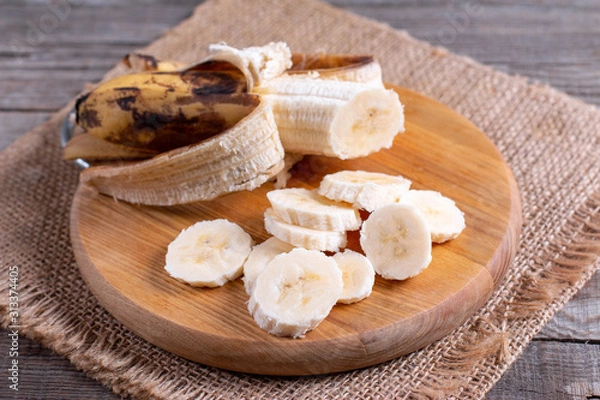 Fototapeta Slices banana on cutting board and wood background