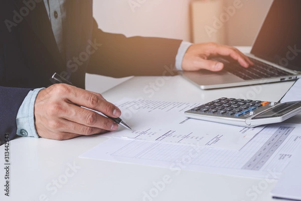 Fototapeta Close up view hands of businessman using calculator and doing accounting with graph and documents on the table.