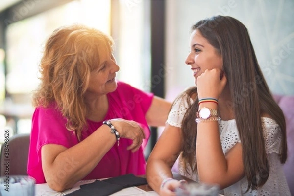 Fototapeta Beautiful mother and daugther sitting at restaurant speaking and smiling