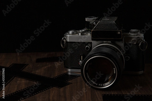 Fototapeta Vintage film camera on a wooden table and black background with film lens and camera shot in low key dark style