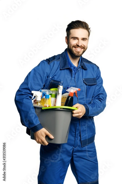 Obraz Attractive young man  in cleaning uniform holding  a bucket of cleaning products in his hands, isolated on white background.