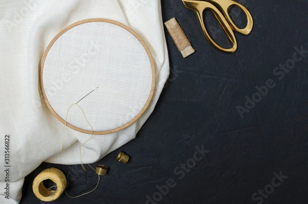 Obraz Top view of tools for embroidering. Golden scissors, threads, thimble, embroidery hoops, clean fabric on the black table