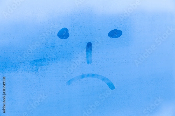 Fototapeta The picture or figure of the sad face on the blue evening or morning window glass with drops 