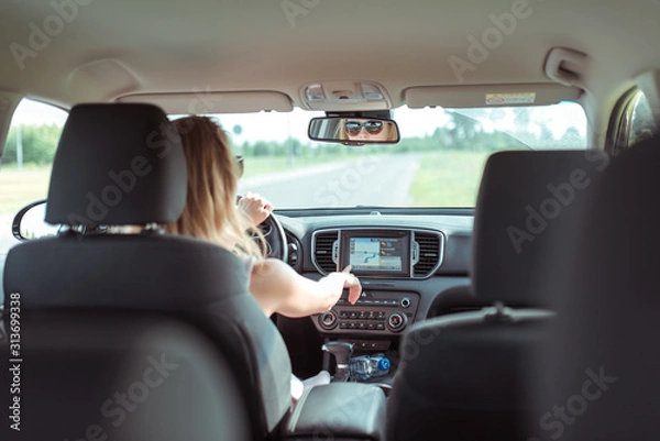 Fototapeta woman in car, sitting behind wheel of a car, selects route application in navigation on touch screen monitor, in summer in car. Girl with glasses, automatic transmission.