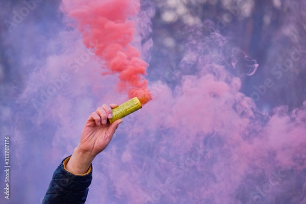 Fototapeta The hand holds a fireworks with a smoke of the color of pink.