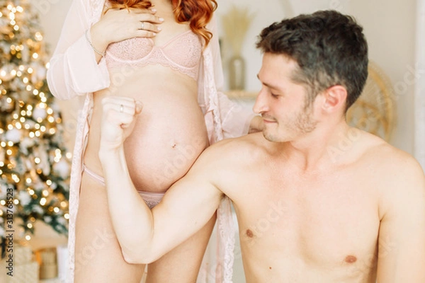 Fototapeta Pregnant in the arms of a bright Studio. Happy couple expecting a baby.