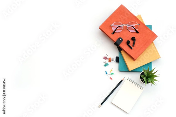 Fototapeta Work space education and back to school concept on white modern table desk with stack of book and blank note pad, earphone, green plant and paper clip, flat lay, Top view with copy space