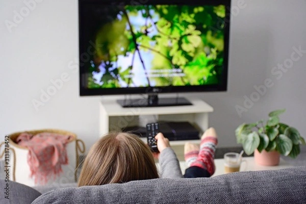 Fototapeta Młoda kobieta ogląda telewizję z napisami, siedząc wygodnie na kanapie w domu w salonie. Natura, zielony, dokumentalny, ekran telewizora