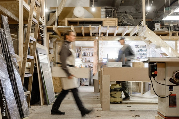 Obraz Exposure photography two unidentified young employees of small woodworking and furniture industry working on new furniture collection. Concept of own small successful production