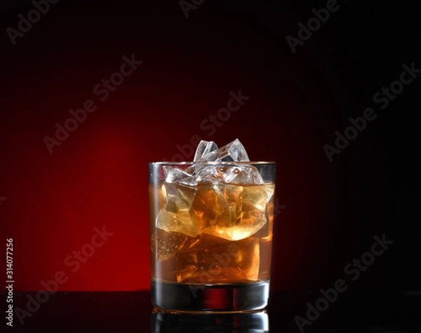 Fototapeta A glass of scotch tape, whiskey, bourbon with ice cubes. Dark background with red, horizontal