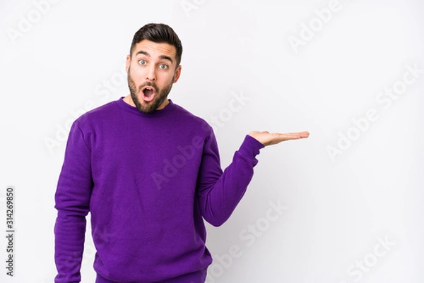 Fototapeta Young caucasian man against a white background isolated impressed holding copy space on palm.