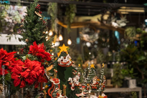Obraz Wooden rocking horse toy surrounded by Christmas tree and red flowers. Christmas decoration at the cafe indoor.