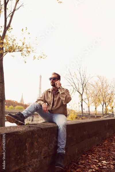 Fototapeta Handsome man using cellphone while enjoying in Paris.