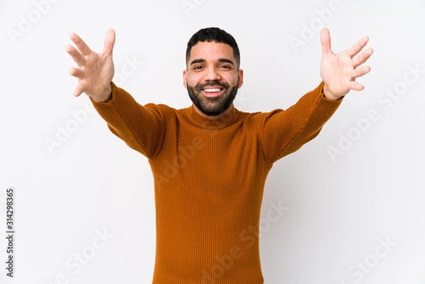 Fototapeta Young latin man against a white background isolated feels confident giving a hug to the camera.