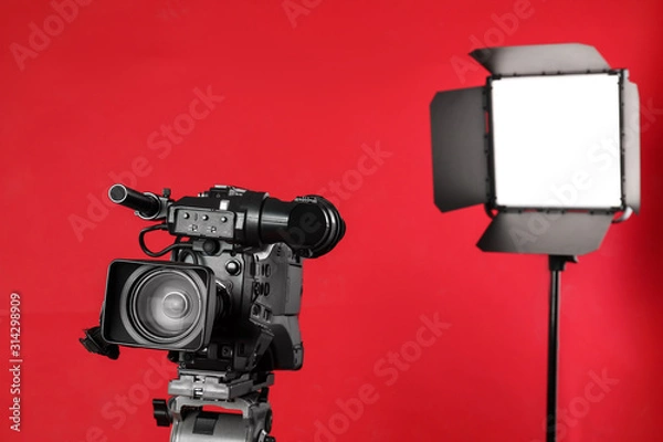 Fototapeta Professional video camera and lighting equipment on red background