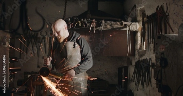 Obraz Young blacksmith with angle grinder in his workshop