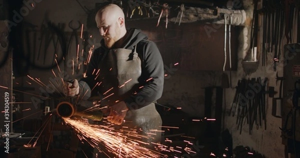 Obraz Young blacksmith with angle grinder in his workshop