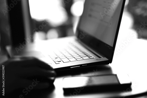 Fototapeta Close up view of laptop and mobile phone with freelancer working on it black and white