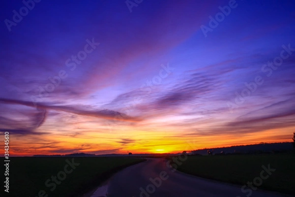 Fototapeta Beautiful multicolored sunset. Cumulonimbus and very colorful stratus in a dramatic sky. Sun disappearing behind a hill.