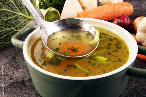 Fototapeta Broth with carrots, onions various fresh vegetables in a pot - colorful fresh clear spring soup. Rural kitchen scenery vegetarian bouillon stock