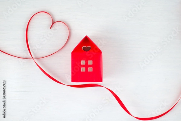 Obraz Red ribbon heart on a white wooden background, red house with a heart shape window in a romantic, valentine, family or wedding concept. Empty space for your text.