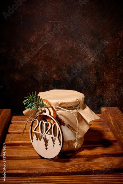 Obraz A jar full of sweet spices is covered with Kraft paper and tied with twine a medallion with the numbers of the new year 2020 is tied to it which stands on a wooden pallet