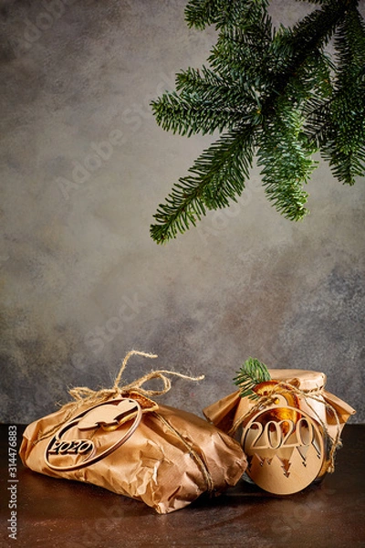 Obraz Gift in craft paper the Bank is covered with craft paper and tied with twine they are tied with medallions in the form of new year symbols a fir mouse and the numbers 2020 above them hangs a branch of