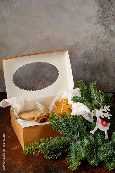 Obraz sweet Christmas gifts cookies, a jar of caramel lie in a gift box next to a spruce branch and a deer toy on a grunge background